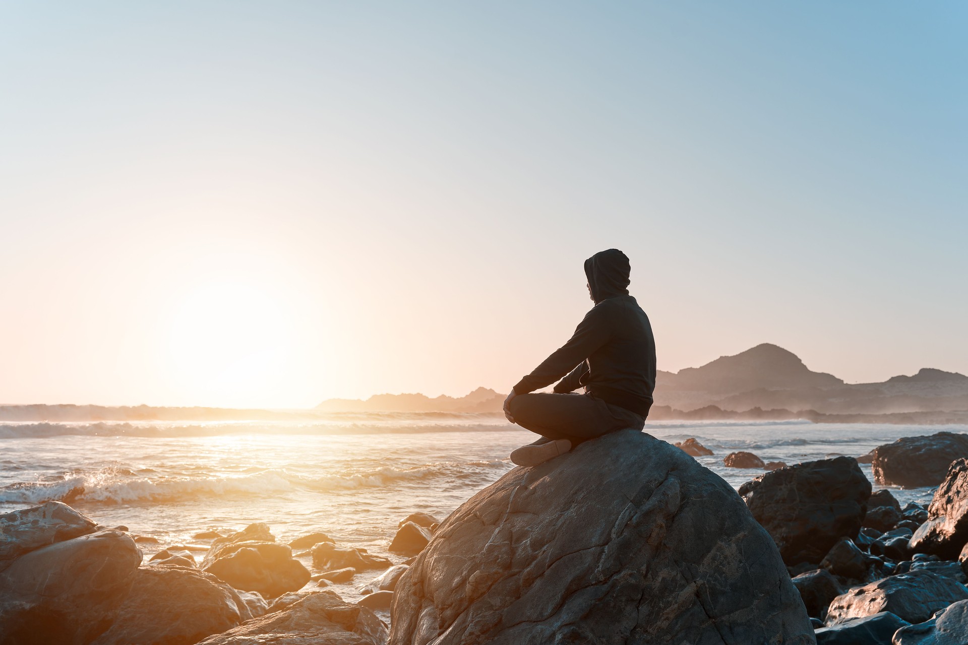 Silhouette d’une personne assise méditant sur le rocher sur la côte au coucher du soleil